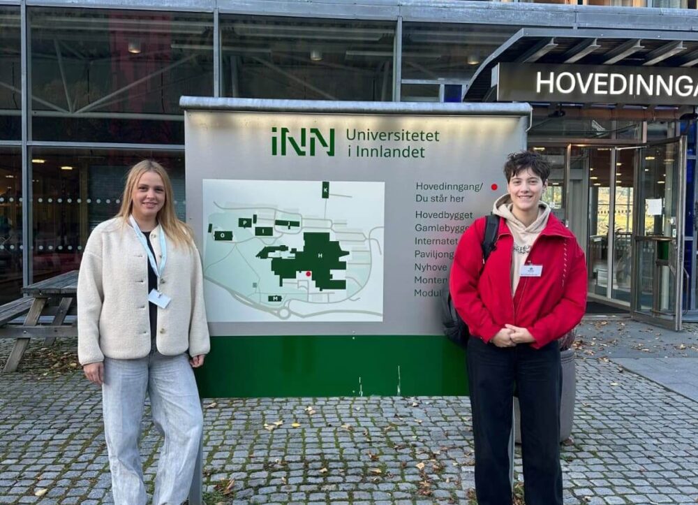 Dos participantes frente a la entrada principal del campus de la University of Inland Norway en Lillehammer.
